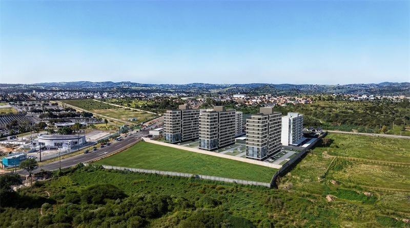 Vista aérea ampla em 3D, com as torres do empreendimento, o terreno e a cidade ao fundo